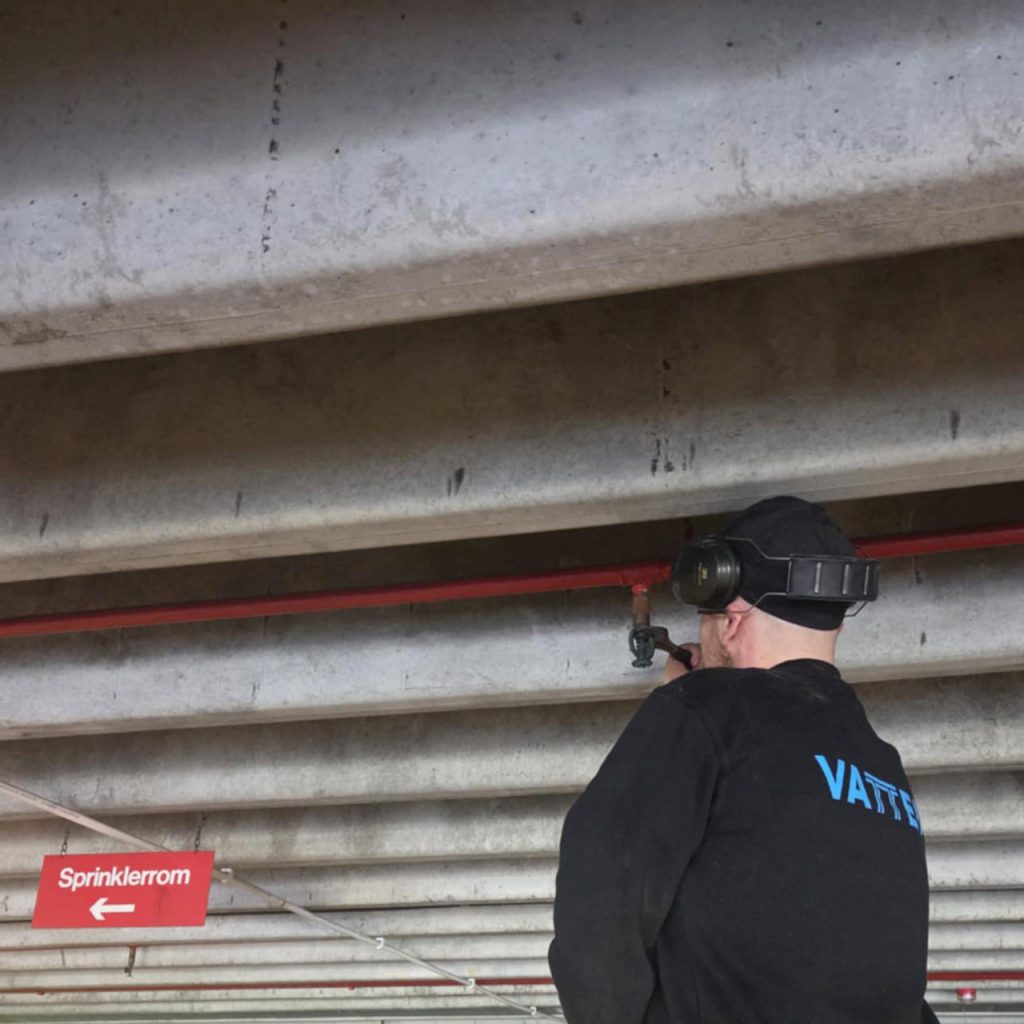 En rørlegger skrur fast en sprinkleranlegg