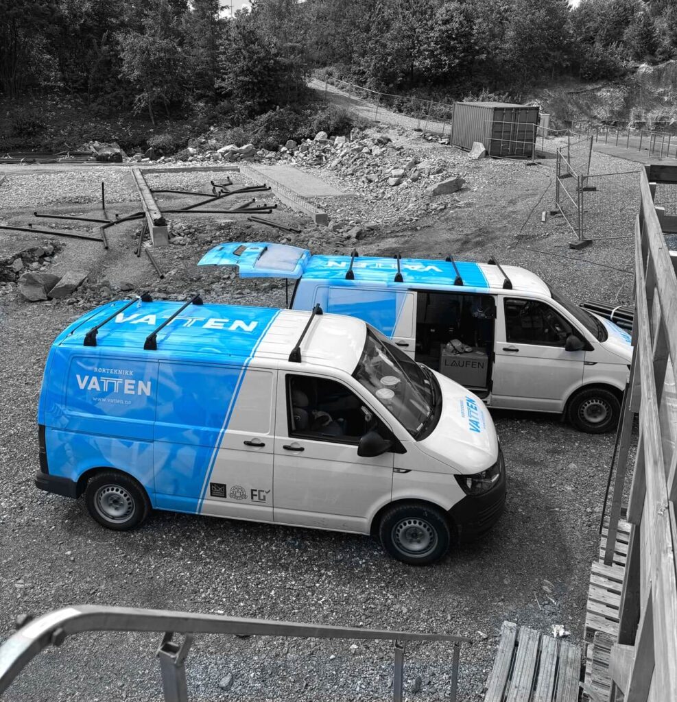 To varebiler på byggeplassen med Vatten-logoen på panseret og blå logodekor på hele baksiden av bilen